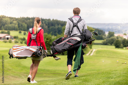 Rear view of couple carrying golf bag
