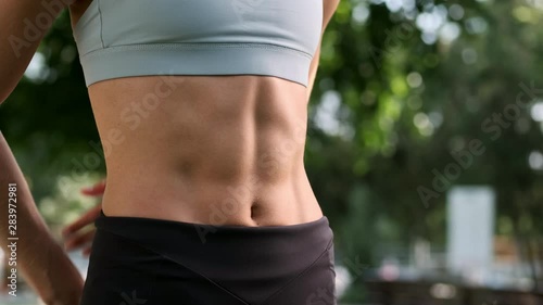 Close up shot of young beautiful woman in sportswear thoughtfully touches abdominal press after workout in city park