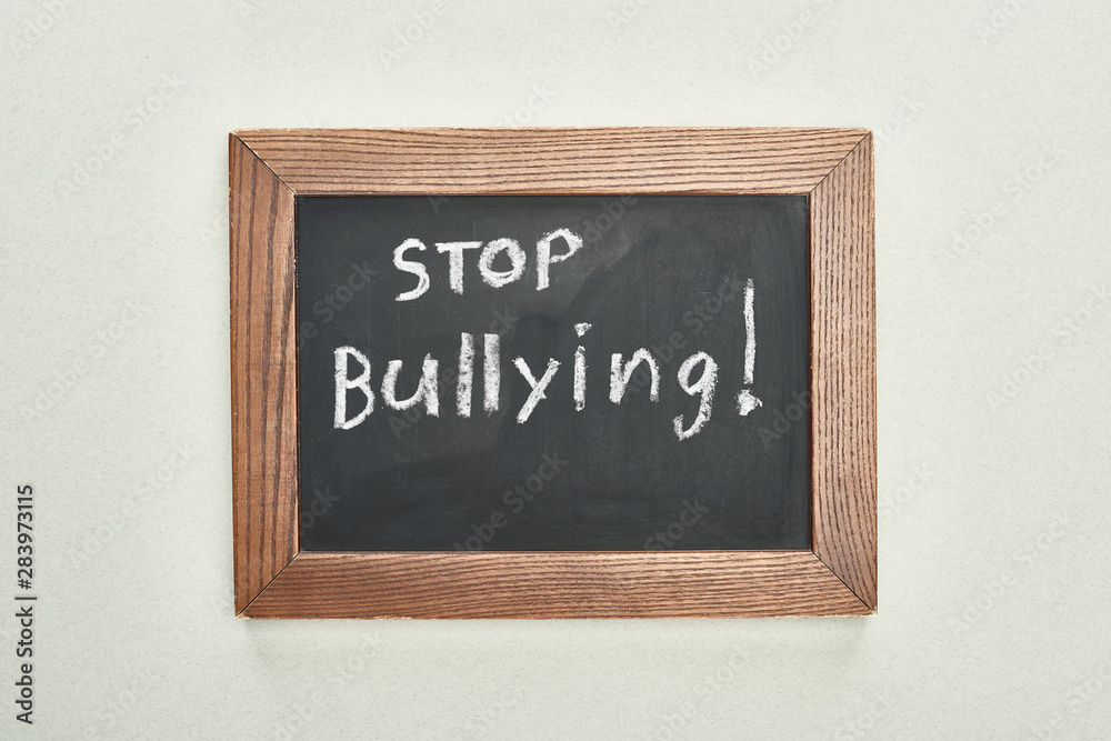 top view of chalkboard in wooden frame with stop bullying lettering on grey background