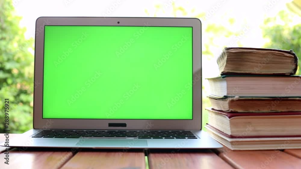 Closeup of modern laptop with green screen and lots old books on background. Technology development. Online education courses. Freelance lifestyle. Study app. Chroma key display. Sunlight. Closeup of modern laptop with green screen and lots old books on background. Technology development. Online education courses. Freelance lifestyle. Study app. Chroma key display. Sunlight.