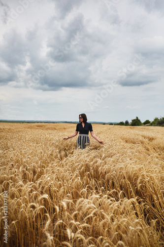 Beautiful young woman in a field of wheat dressed in a stylish dress and glasses