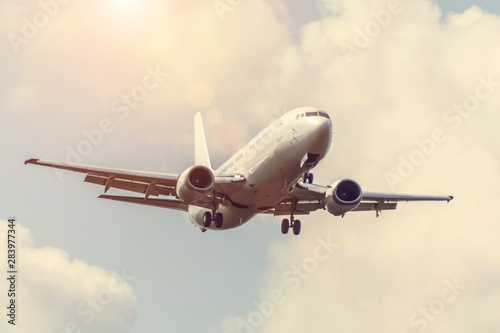 Sky with clouds and sun with a warm shade  reflected glare light  and passenger airplane landing approach airport.