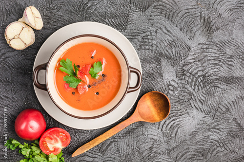 Spanish cold gazpacho soup with tomatoes, pepper, garlic and fresh herbs in a dark plate on black background top view with copyspace
