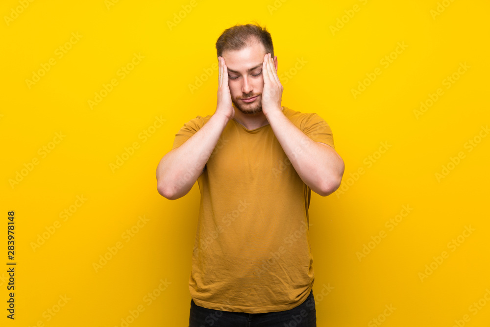 Blonde man over isolated yellow wall with headache Blonde man over isolated yellow wall with headache