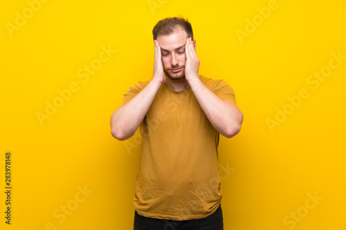 Blonde man over isolated yellow wall with headache
