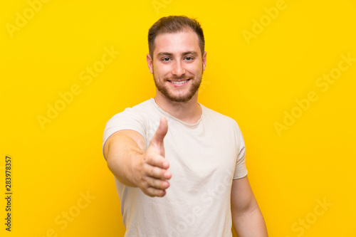 Handsome man over yellow background handshaking after good deal