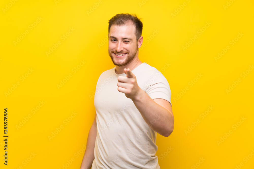 Handsome man over yellow background points finger at you Handsome man over yellow background points finger at you