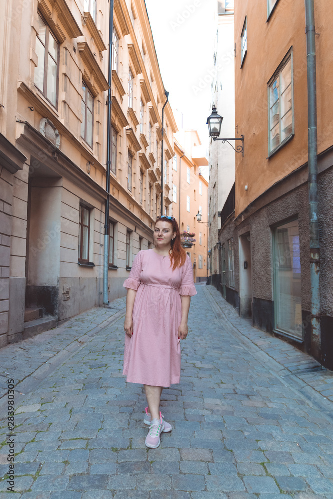 A cheerful woman on the street walks along the narrow streets of Stockholm in the sunlight