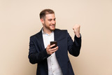 Blonde man over isolated background with phone in victory position