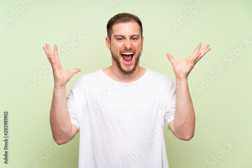 Handsome man over green background unhappy and frustrated with something