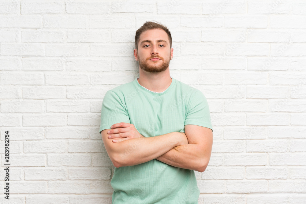 Blonde man over brick wall keeping arms crossed Blonde man over brick wall keeping arms crossed