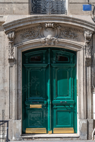 Classical architecture entrance with door painted in bright green color and golden plates on door panels. Elegant doorway of retro stone building with relief elements. Facade of house in Paris France