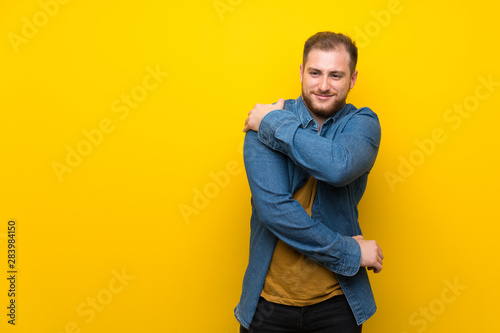 Blonde man over isolated yellow wall suffering from pain in shoulder for having made an effort © luismolinero