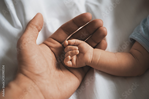 Close-up small hands of baby is lying in men of his father hands, concept of caring, fatherhood photo