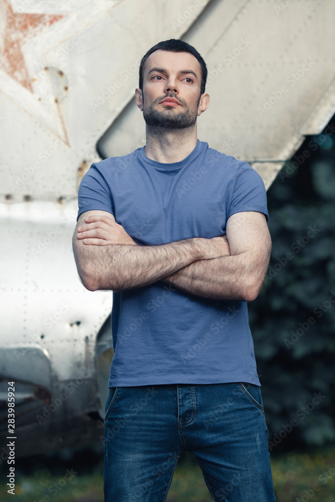 True masculinity concept. Portrait of bearded middle-aged charismatic man posing with crossed hands over old war plane. Text-space. Grunge, retro style. Outdoor shot True masculinity concept. Portrait of bearded middle-aged charismatic man posing with crossed hands over old war plane. Text-space. Grunge, retro style. Outdoor shot