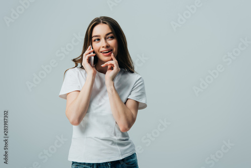 cunning beautiful girl in white t-shirt talking on smartphone isolated on grey