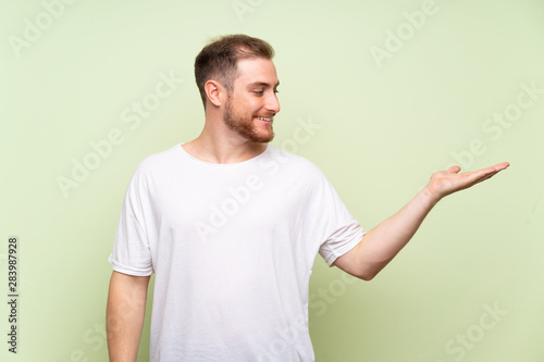 Handsome man over green background holding copyspace imaginary on the palm