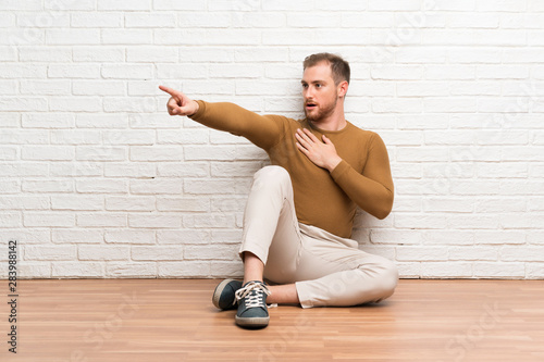 Blonde man sitting on the floor pointing finger to the side