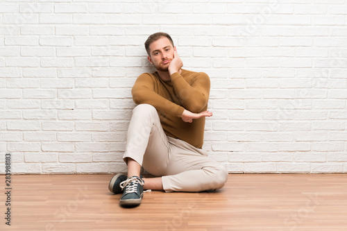 Blonde man sitting on the floor unhappy and frustrated