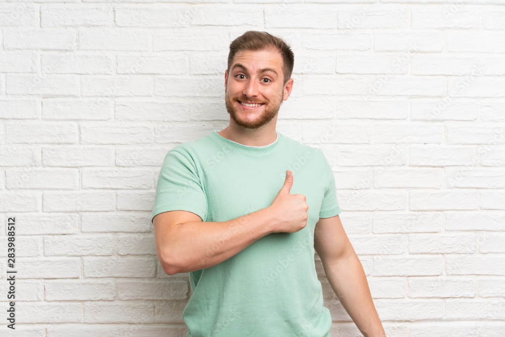 Blonde man over brick wall giving a thumbs up gesture Blonde man over brick wall giving a thumbs up gesture