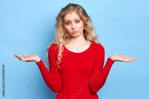 Puzzled hesitant girl with long fair hair dressed casually, shrugs shoulders as she doesn t know answer being clueless and uncertain.facial expression, attitude concept photo