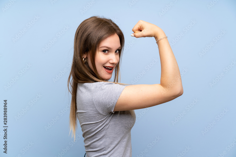 Teenager girl over isolated blue wall doing strong gesture