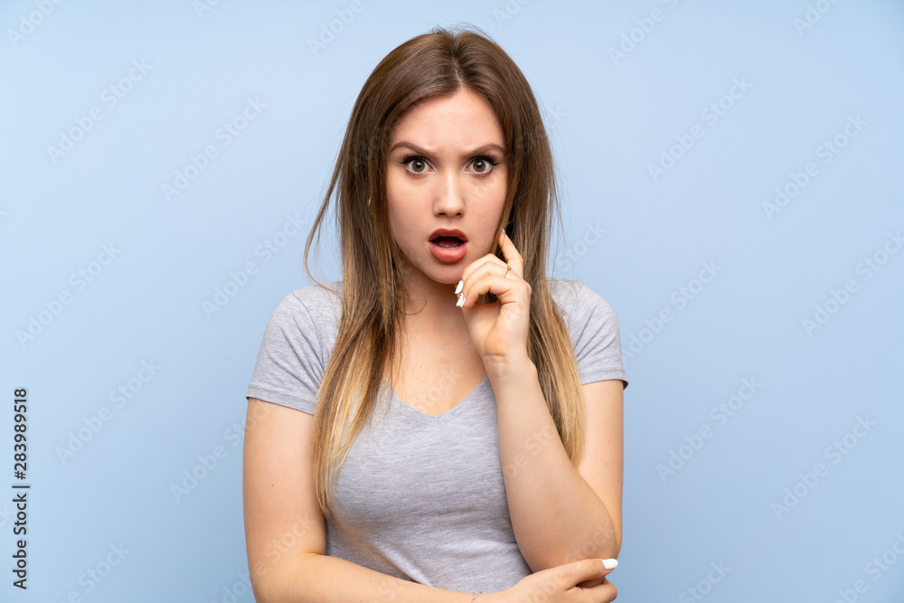 Teenager girl over isolated blue wall surprised and shocked while looking right Teenager girl over isolated blue wall surprised and shocked while looking right