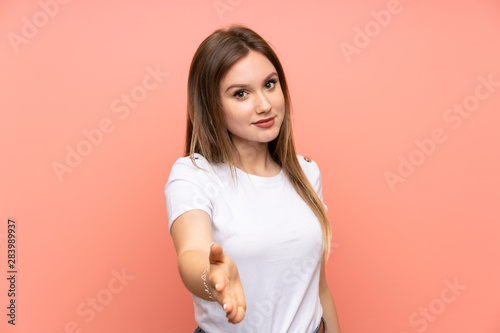 Teenager girl over isolated pink wall handshaking after good deal