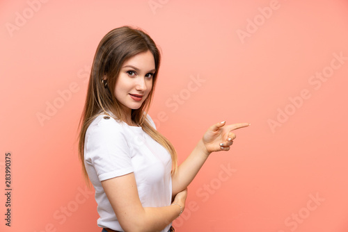 Teenager girl over isolated pink wall pointing finger to the side
