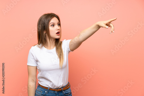 Teenager girl over isolated pink wall pointing away