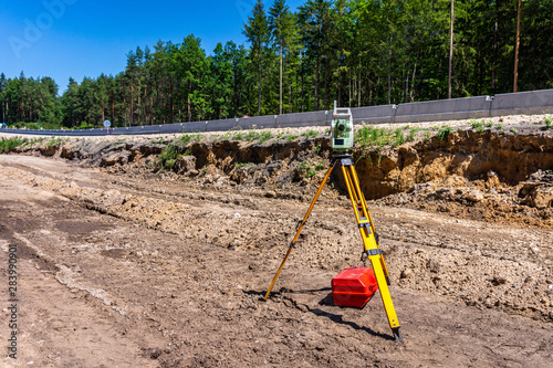 Surveyor engineer with equipment (theodolite or total positioning station) on the construction site of the road, highway or building in background