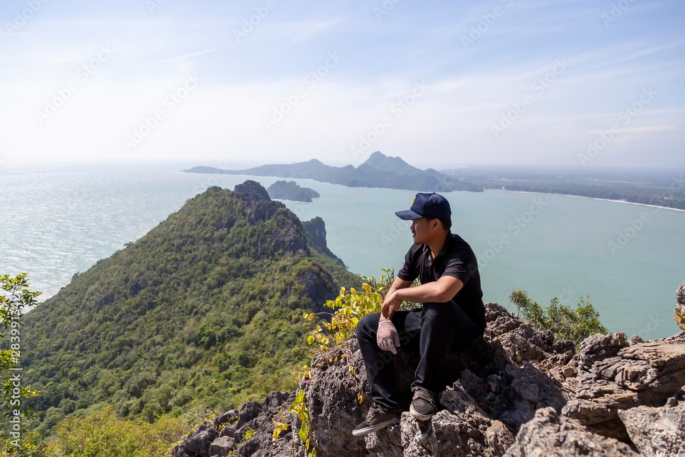 Asian men are sitting on the top of the mountain and the view of the sea in Prachuap Khiri Khan Province, Thailand. Men in black dress looking at the view of the sea on the hilltop.