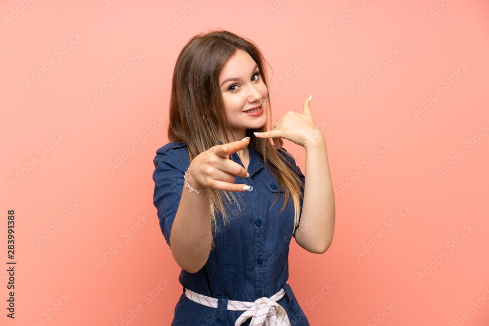 Teenager girl over isolated pink background making phone gesture and pointing front Teenager girl over isolated pink background making phone gesture and pointing front