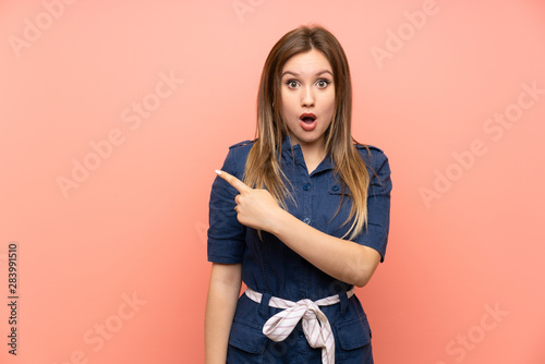 Teenager girl over isolated pink background surprised and pointing side