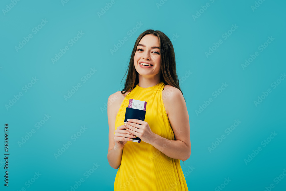 happy brunette girl in yellow dress holding passport with air ticket isolated on turquoise happy brunette girl in yellow dress holding passport with air ticket isolated on turquoise