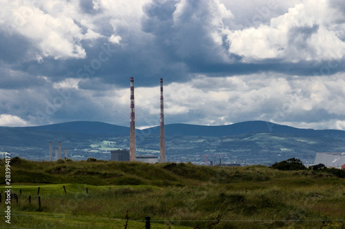 The twin towers of Poolbeg Power Station with the Dublin mountains in the background and the green grass of Bull Island causeway in the foreground.