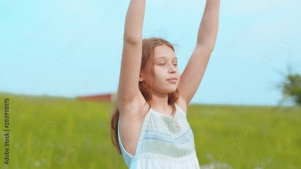 Close up rotation view of adorable smiling little teenage girl in light summer dress raising her hands, enjoying fresh air and wind on green meadow background. Happiness concept Close up rotation view of adorable smiling little teenage girl in light summer dress raising her hands, enjoying fresh air and wind on green meadow background. Happiness concept