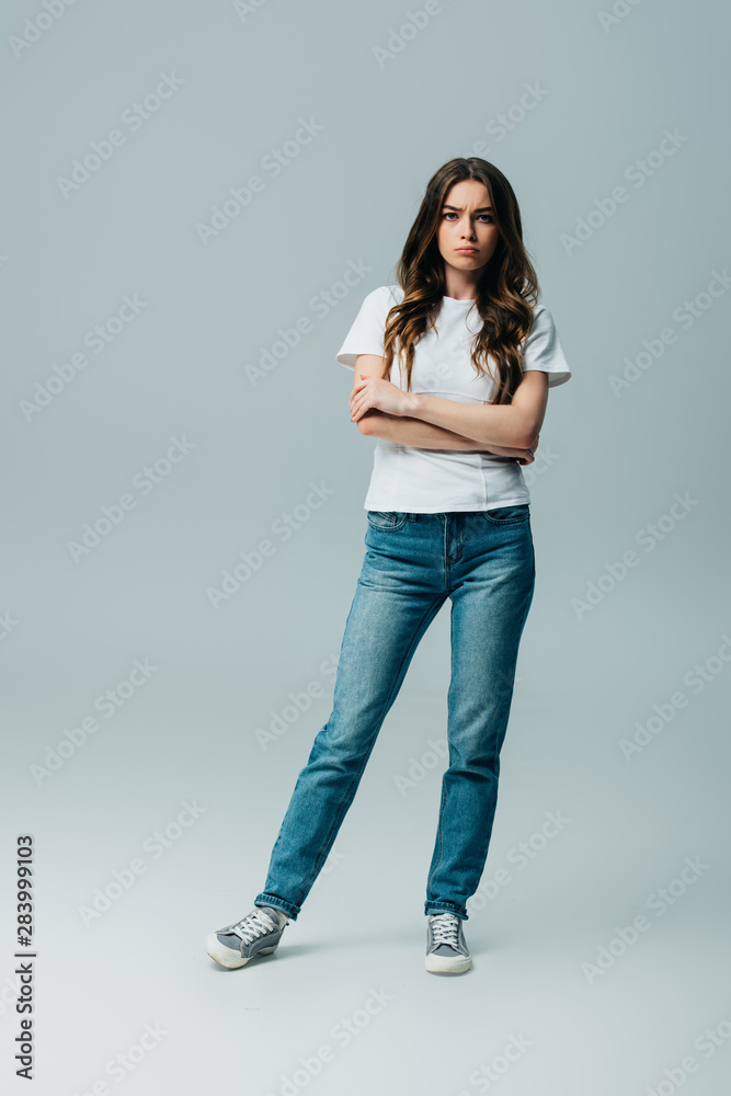 sad beautiful girl in white t-shirt and jeans with crossed arms isolated on grey sad beautiful girl in white t-shirt and jeans with crossed arms isolated on grey