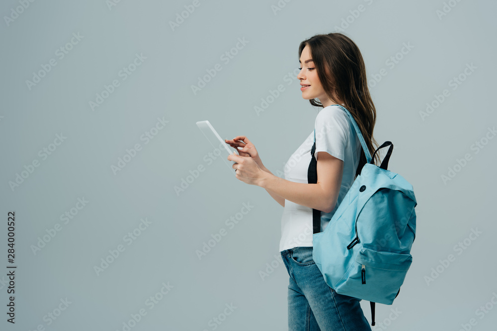 side view of pretty girl with blue backpack using digital tablet isolated on grey - obrazy, fototapety, plakaty 