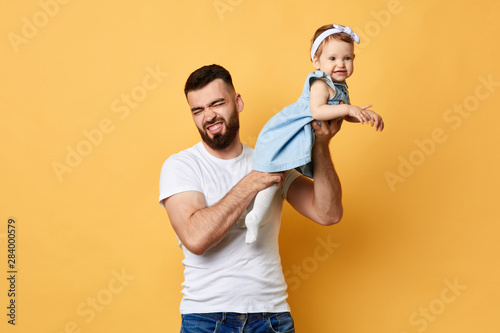 Young unhappy bearded dad holding daughter in hands, stink coming from his daughter. close up photo. isolated backgrounf. difficult parenthood.