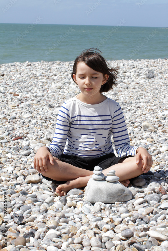eyes closed child sitting for relaxation and mindfulness on beach