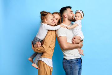 caring parents hugging their children, expressing love, warm feeling. close up photo. isolated blue background. studio shot