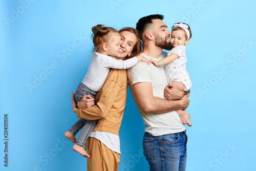 caring parents hugging their children, expressing love, warm feeling. close up photo. isolated blue background. studio shot