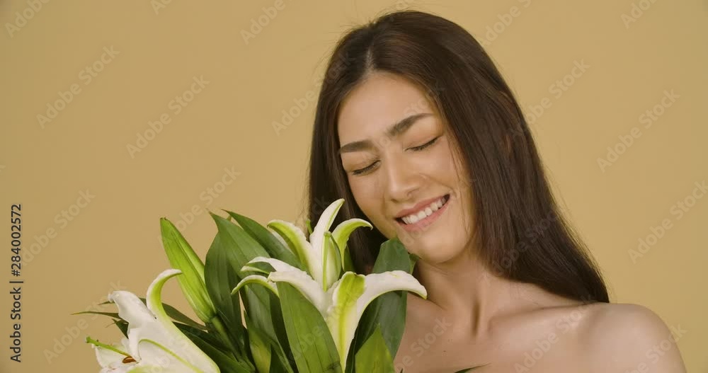 Studio Portrait Of A Beautiful Young Asian Woman With Health Skin Holding and smelling Lily Flower In Her Hand, and happily smiling straight to camera. Romantic atmosphere, being in love. Studio Portrait Of A Beautiful Young Asian Woman With Health Skin Holding and smelling Lily Flower In Her Hand, and happily smiling straight to camera. Romantic atmosphere, being in love.