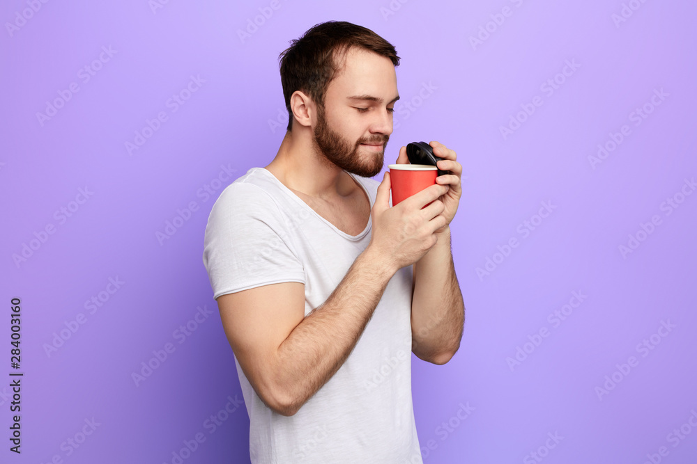 Man holding disposable plastic cup with coffee and enjoys the aroma. close up side view photo. isolated blue background, time for coffee break Man holding disposable plastic cup with coffee and enjoys the aroma. close up side view photo. isolated blue background, time for coffee break