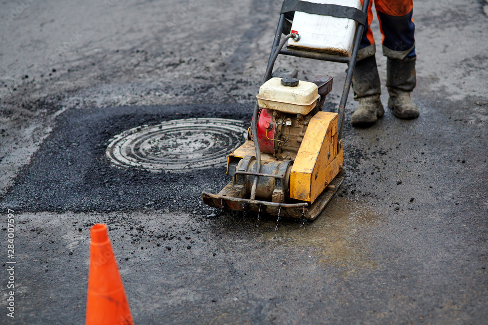 Construction worker in uniform operate vibratory plate compactor