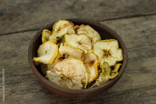 Apple chips in a brown clay bowl on wooden background