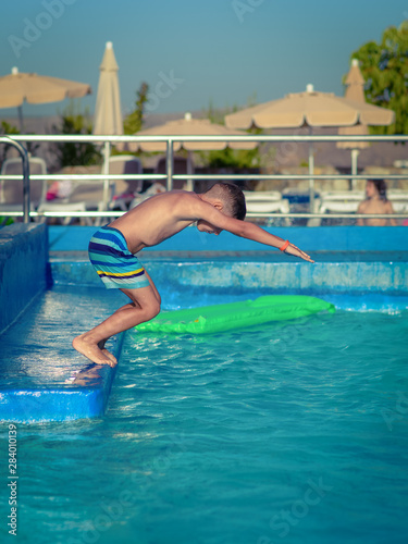 European boy in striped swimming shorts is diving to the swimming pool. He is enjoying his summer holidays in Spain.