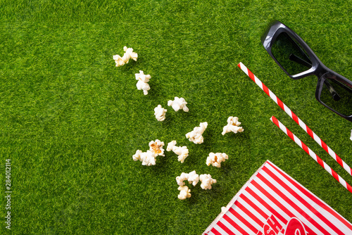Packing with popcorn straws for soda on a green lawn with 3D glasses for watching a movie. Grass Watching films about nature. In parks. Recreation and entertainment. background