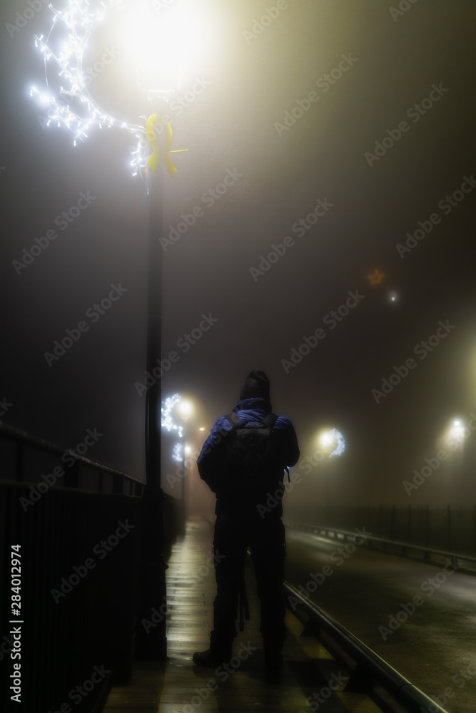 Man with his back in a hat walking on a bridge and entering the fog